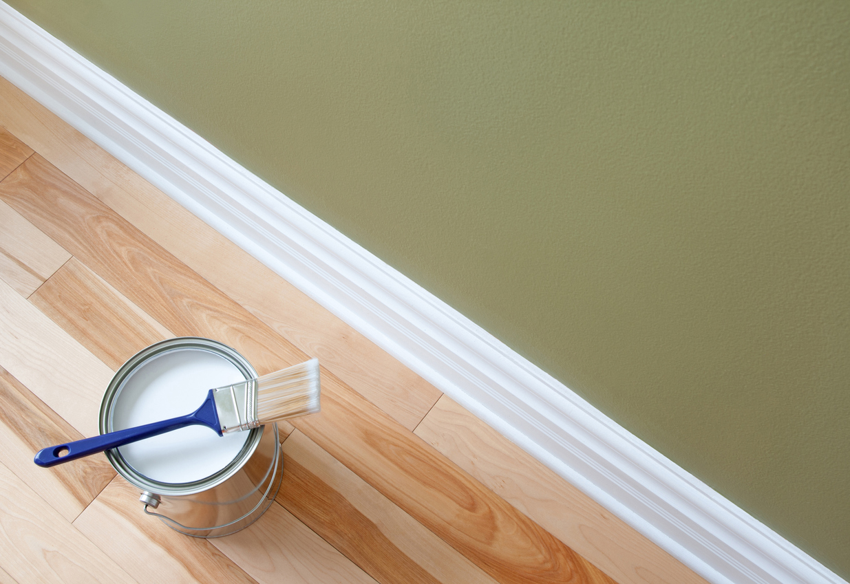 Newly opened can of white paint and paintbrush on wooden floor.